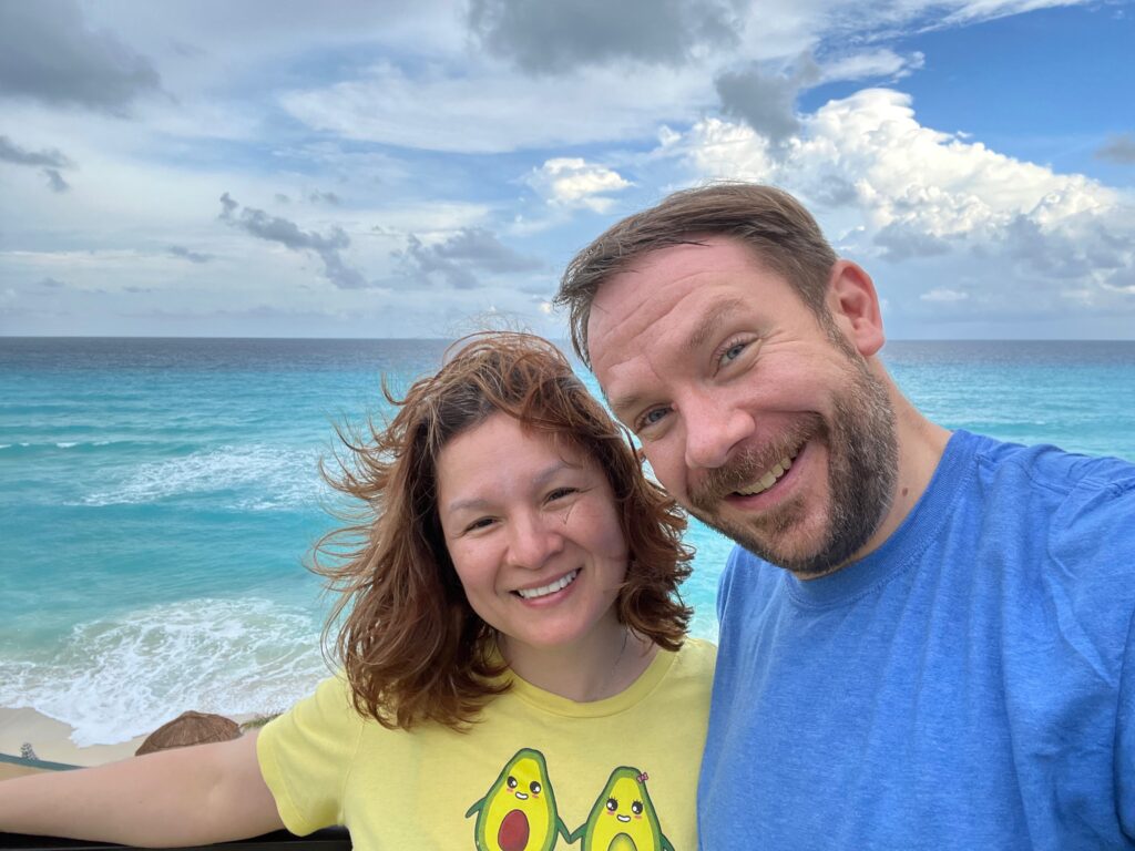 Jossy Salguero and Dan Smith smiling at the camera standing above a beach in Latin America